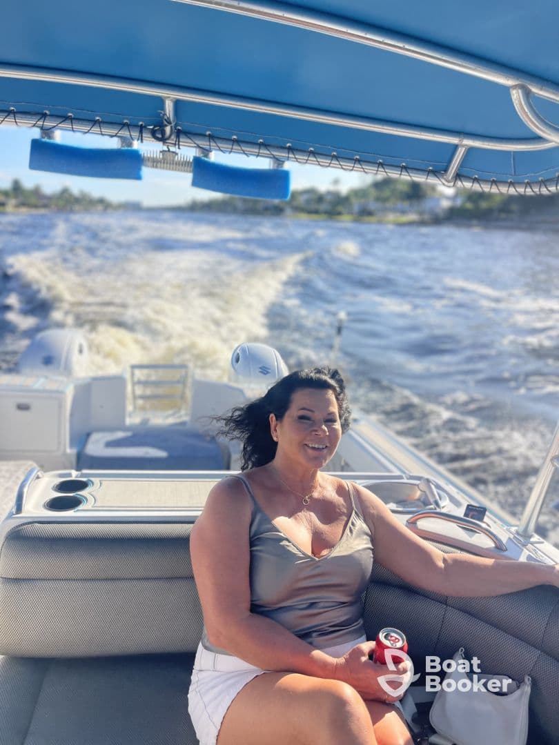 A woman enjoys a sunny day on a boat, smiling and holding a drink while cruising through the water — a perfect moment for relaxation and fun on the water.