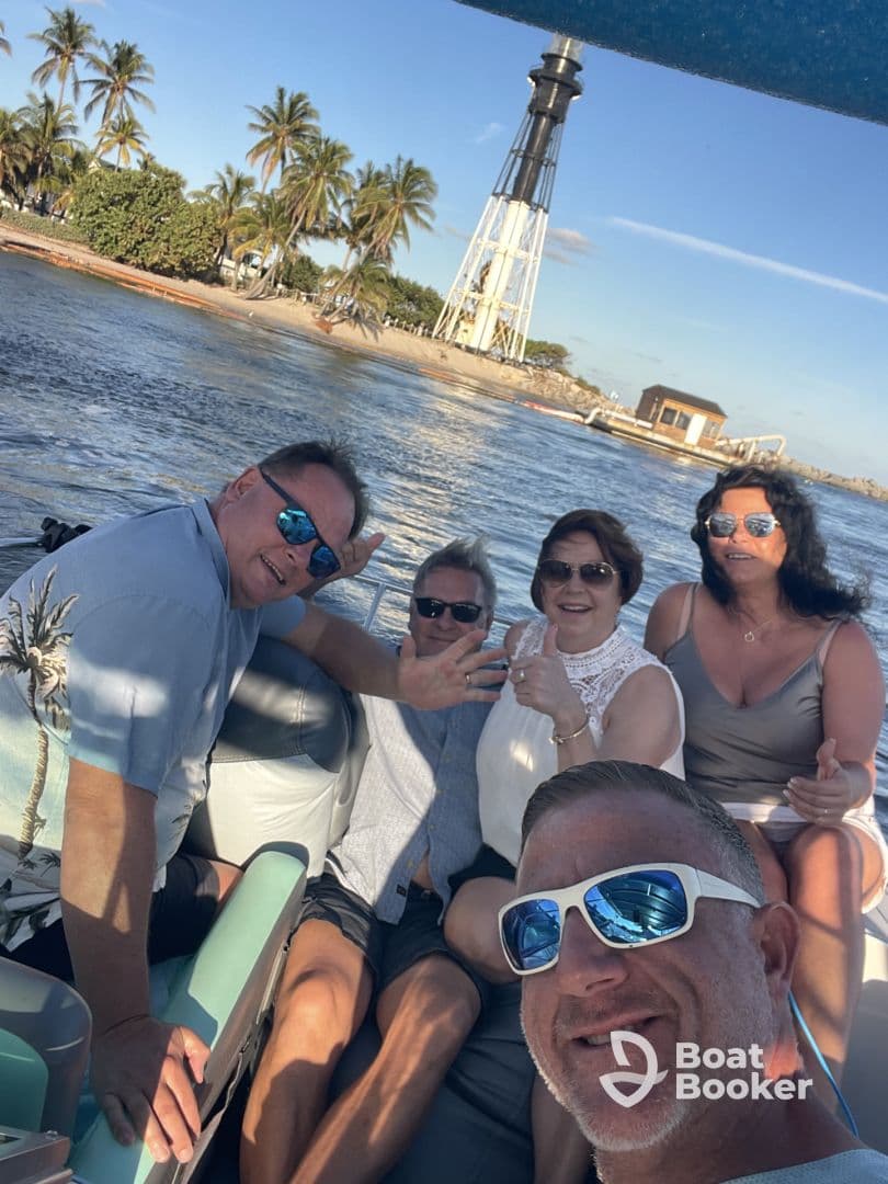 A cheerful group enjoys a day on the water, posing for a selfie with a lighthouse in the background — perfect for memorable boating adventures.