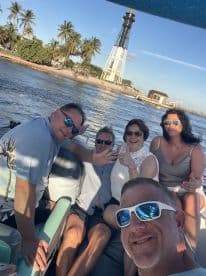 A cheerful group enjoys a day on the water, posing for a selfie with a lighthouse in the background — perfect for memorable boating adventures.