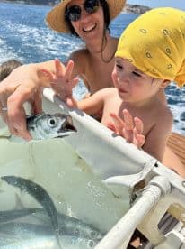 A joyful moment as a child interacts with a fish while fishing on a boat, showcasing the excitement of wildlife encounters at sea.