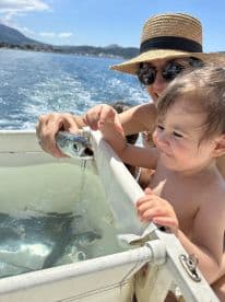 A child and an adult interact with a fish caught during a boating trip, showcasing a memorable wildlife experience on the water.