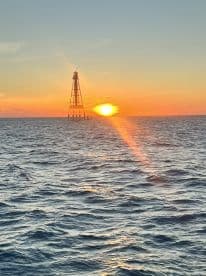 A stunning sunset over the ocean with a lighthouse silhouetted against the vibrant sky, perfect for capturing the beauty of coastal adventures.