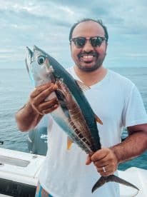 A proud angler displays his catch of the day, showcasing a vibrant fish against the backdrop of the open ocean — a perfect moment for fishing enthusiasts.
