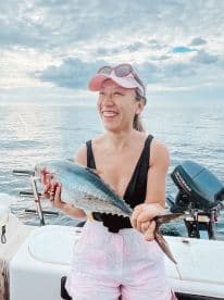 A joyful woman proudly holds her catch while fishing on the open ocean, capturing the thrill of a successful day on the water.