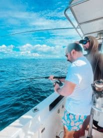 Two friends enjoy a fishing trip on the open ocean, showcasing the thrill of reeling in a catch while surrounded by stunning blue waters.