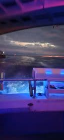 A view from inside the cabin of a boat at night, showcasing the helm area illuminated with colorful lights, perfect for evening cruises.