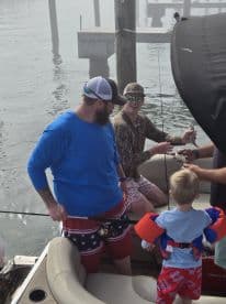 A family enjoys a fishing trip on a boat, with a child in a life jacket excitedly watching as adults catch fish — a perfect day on the water.