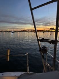 A serene sunset view from the deck of a boat, showcasing the tranquil waters and distant lights of the harbor — perfect for evening cruises.