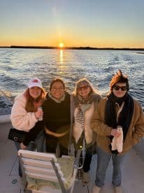 A joyful group of friends poses for a photo on a boat during sunset, capturing the essence of a perfect evening on the water.