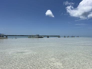 A serene sandbar scene with boats anchored in shallow waters, where guests enjoy swimming and relaxing under the sun — a perfect getaway for water enthusiasts.