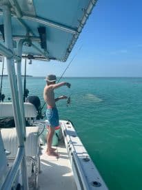 A young man enjoys a day of fishing on a boat, showcasing his catch against the stunning turquoise waters — a perfect moment for fishing enthusiasts.