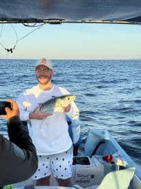 A proud angler holds up a freshly caught fish aboard a boat, showcasing the thrill of fishing in open waters.