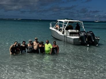 A cheerful group enjoys a day at the beach, partially submerged in clear waters with their boat anchored nearby — perfect for a fun-filled day on the water.
