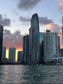 A scenic view of Miami's skyline at sunset, showcasing the city's towering buildings reflected in the water.