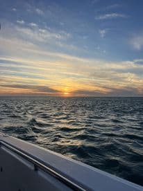 A serene sunset view from the deck of a boat, showcasing the tranquil ocean waves and vibrant sky — perfect for romantic evening cruises.