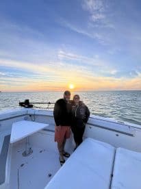 A couple enjoys a romantic sunset on a boat, capturing a perfect moment together against a stunning backdrop of vibrant colors on the water.