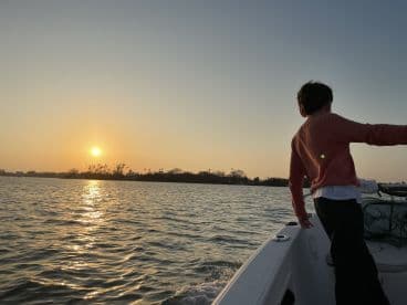 A young person enjoys a serene sunset view from the boat, capturing the beauty of the moment on the water.
