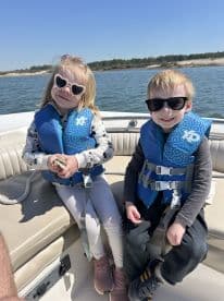 Two children enjoy a sunny day on a boat, wearing life jackets and sunglasses, capturing the joy of family outings on the water.
