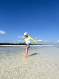 A child joyfully splashes in shallow waters at the beach, capturing the essence of fun and adventure in a tropical paradise.