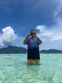 A man captures the stunning scenery while wading in crystal-clear waters, showcasing a perfect day of relaxation and exploration in a tropical paradise.