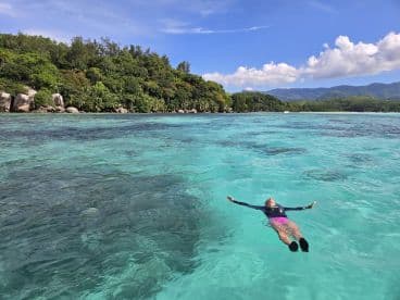 A person floats peacefully in the crystal-clear waters near a lush island, showcasing the serene beauty of tropical destinations perfect for relaxation and adventure.