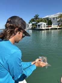A fisherman holds a freshly caught fish while enjoying a sunny day on the water, showcasing the thrill of fishing adventures.