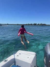 A child joyfully jumps into the clear waters with a pool noodle, capturing the essence of fun water activities during a boating adventure.