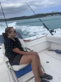 A woman enjoys a fishing trip aboard a boat, taking in the scenic ocean views while waiting for a catch.