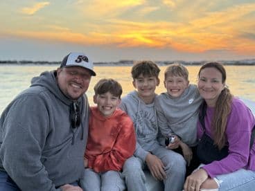 A joyful family poses for a photo on a boat during sunset, capturing a memorable moment of togetherness and fun on the water.