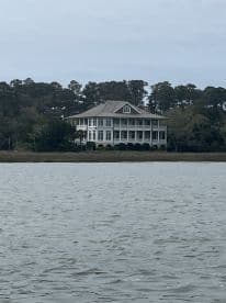 A distant view of a large house by the water, surrounded by trees. The image lacks clarity and detail.