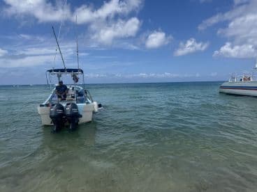 A man stands on a boat in shallow waters, enjoying a day of fishing under a bright blue sky — a perfect scene for water enthusiasts.