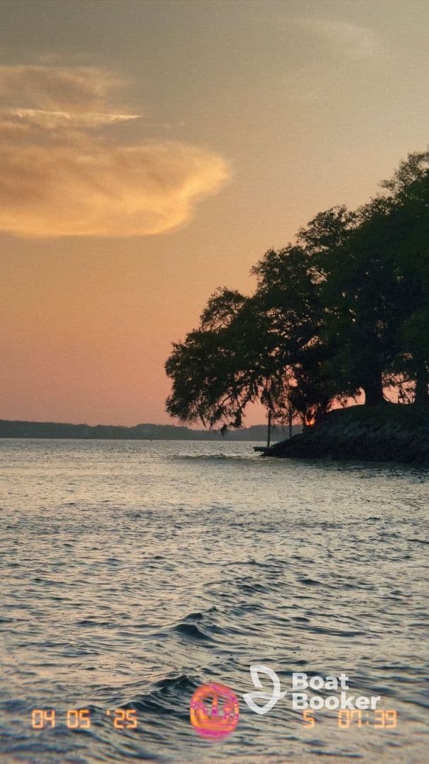 A scenic view of a sunset over water, featuring trees along the shoreline. The image captures a tranquil moment but lacks clarity.