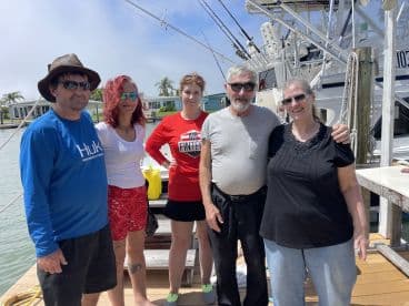 A cheerful group poses together on the dock beside a fishing boat, capturing a memorable moment before their adventure on the water.