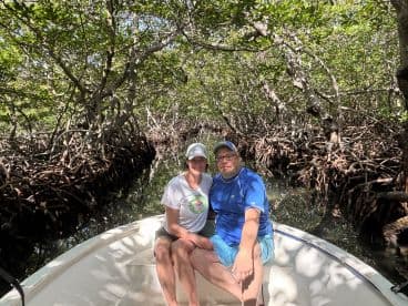 A couple enjoys a serene moment in a small boat surrounded by lush mangroves, perfect for exploring nature's beauty.