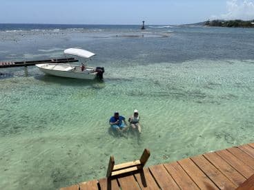 A couple enjoys a refreshing swim in crystal-clear waters next to a small boat, creating a perfect beach getaway atmosphere.