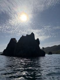 A stunning view of rocky islands silhouetted against a bright sun and textured clouds, capturing the serene beauty of coastal landscapes.