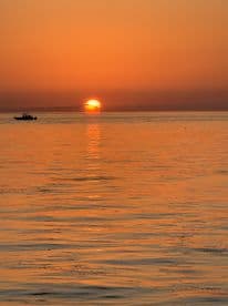 A stunning sunset over the water with a silhouette of a boat in the foreground, capturing the serene beauty of evening cruises.