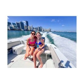 Two friends enjoy a sunny day on a boat, capturing the vibrant city skyline in the background — a perfect summer adventure on the water.