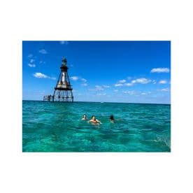A group of friends enjoys a refreshing swim in the crystal-clear waters near a historic lighthouse, capturing the essence of a perfect day at the beach.
