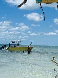 A group enjoys a fun day at the beach, with some swimming in the shallow water while a yellow boat is anchored nearby — perfect for family outings and water adventures.