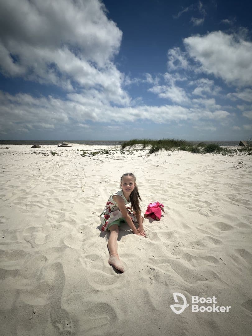 A young girl enjoys a sunny day on the beach, playing in the sand and smiling for the camera — a perfect moment of childhood joy by the water.
