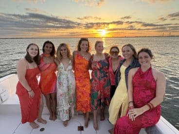 A group of friends poses together on a boat at sunset, celebrating their time on the water with vibrant outfits and smiles — perfect for memorable gatherings and special occasions.