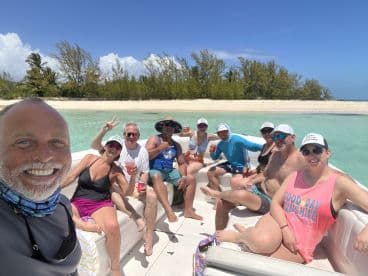 A lively group enjoys drinks on a boat, soaking up the sun and celebrating together against a beautiful beach backdrop — perfect for memorable outings and fun in the sun.