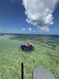 A group enjoys a relaxing day on a floating mat in crystal-clear waters, perfect for sunbathing and fun in the sun.