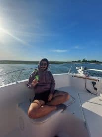 A man enjoys a refreshing drink while relaxing on the deck of a boat under the bright sun — a perfect moment for leisure on the water.