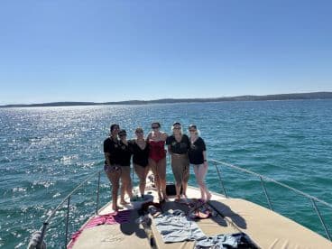 A cheerful group of friends poses on the bow of a boat, enjoying a sunny day on the water — perfect for celebrations and memorable outings.