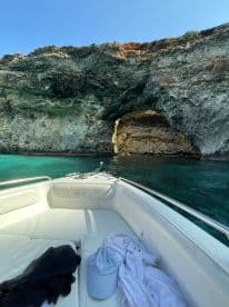 A serene view from the deck of a boat, showcasing the stunning rocky coastline and clear turquoise waters, perfect for exploring hidden caves and enjoying a day on the water.