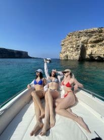 Three friends enjoy a sunny day on a boat, showcasing their beachwear against a stunning coastal backdrop — perfect for summer adventures and fun on the water.
