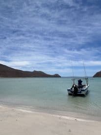 A small boat is docked in calm waters with a scenic backdrop of mountains and a clear blue sky, perfect for exploring coastal destinations.
