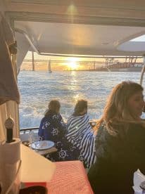 A group enjoys a cozy sunset view from the deck of a boat, wrapped in blankets, creating a perfect atmosphere for dining and relaxation on the water.